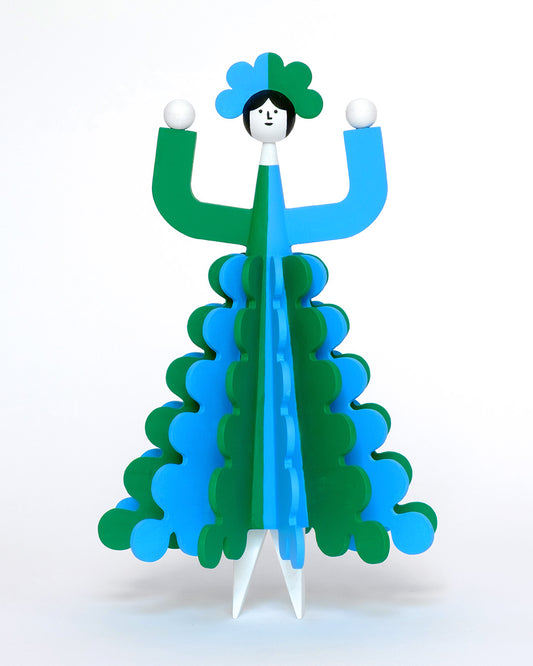 A colourful wooden sculpture with a green and blue stripey 3D skirt and a matching headdress with white legs on a plain white background.