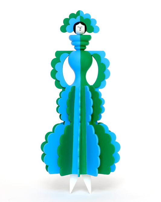 A colourful wooden sculpture with a blue and green stripey dress and a matching headdress with white legs on a plain white background.