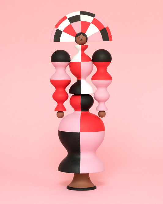 A colourful sculpture with a white, red, black and pink stripey curved body with a matching headdress on a plain pink background.