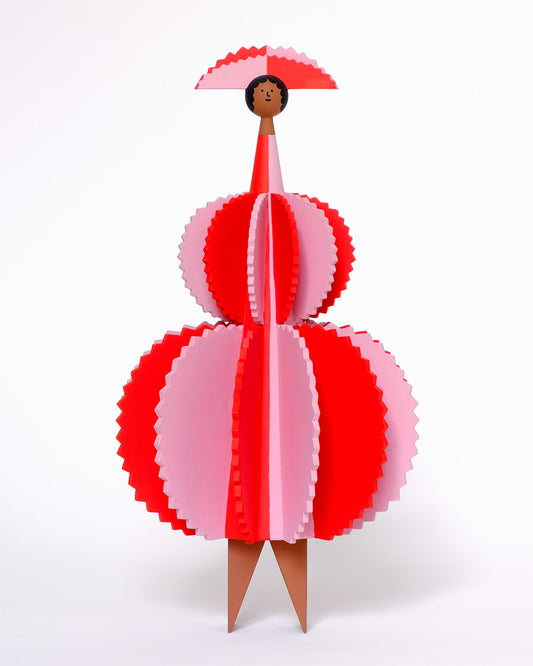 A colourful wooden sculpture with a red and pink stripey 3D round dress and a matching headdress with brown legs on a plain white background.