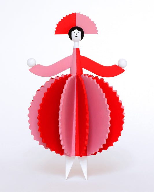 A colourful wooden sculpture with a pink and red stripey 3d round dress and a matching headdress and white legs on a plain white background.