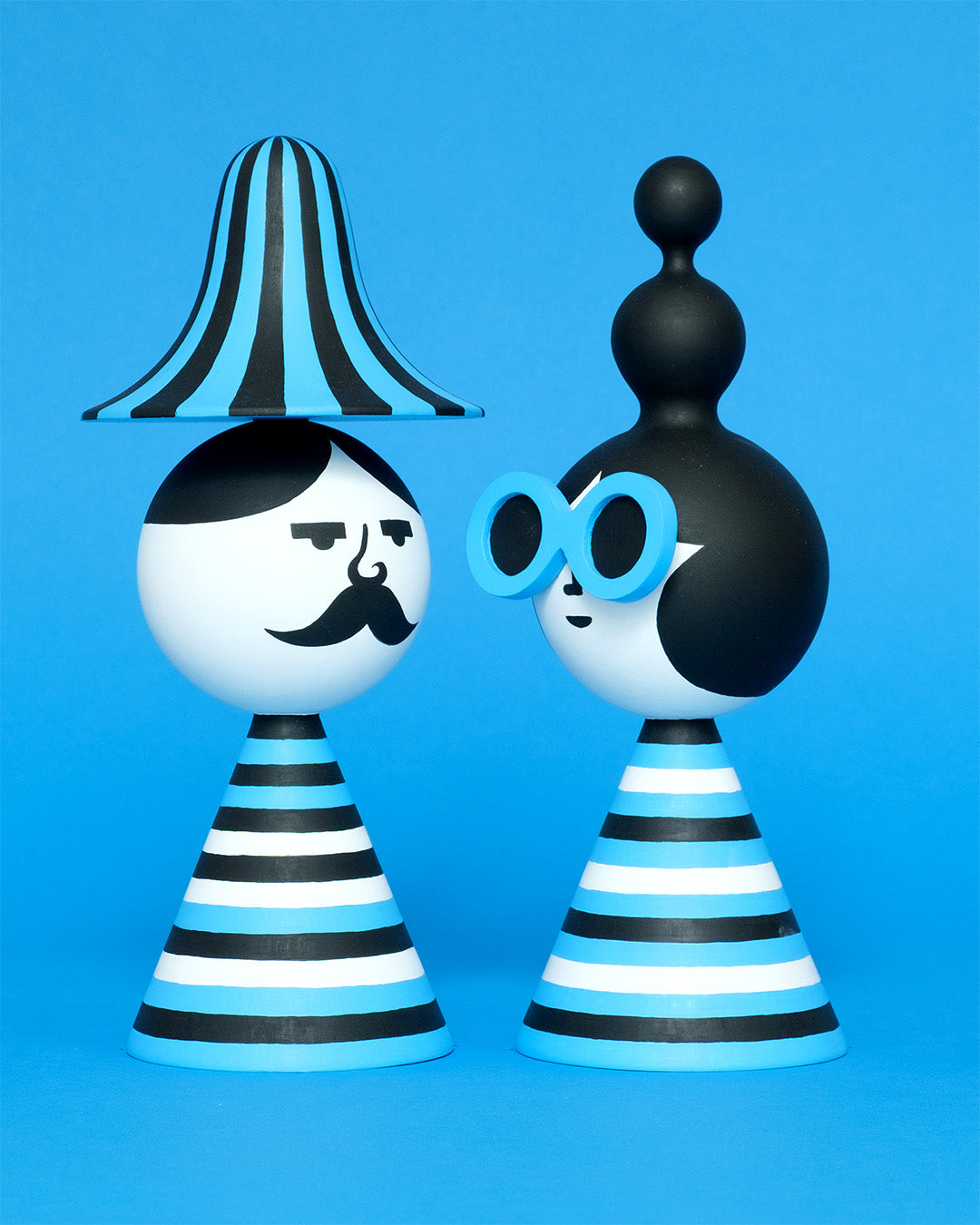 A pair of blue, white, and black stripey bust figures with a stripey hat and blue sunglasses on a plain blue background.