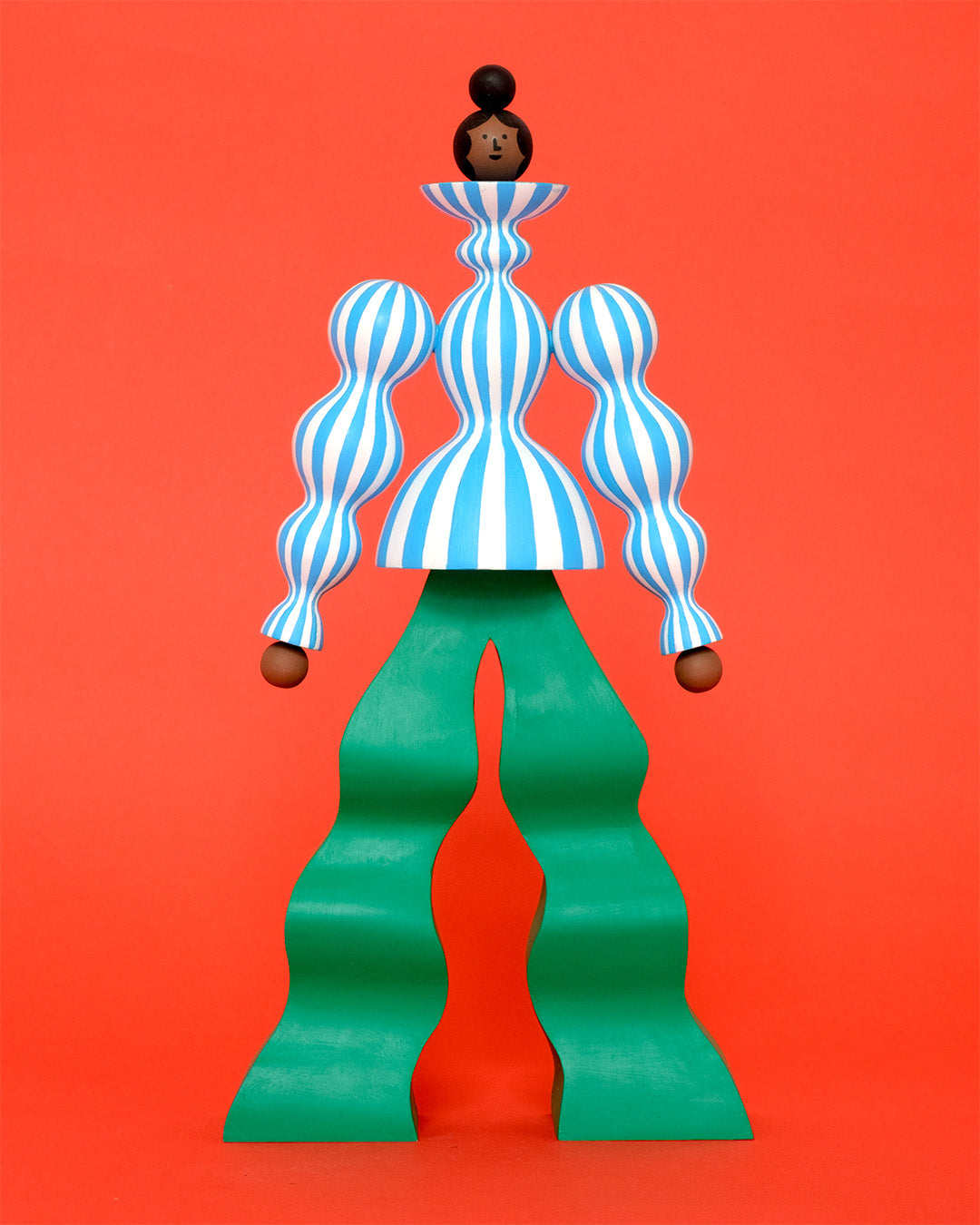 A colourful sculpture with a blue and white stripey body with wavy green trousers on a plain orange background.