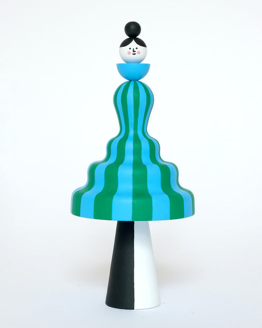 Colourful sculpture of a figure made from a green and blue stripey body with white and black legs on a plain white background.