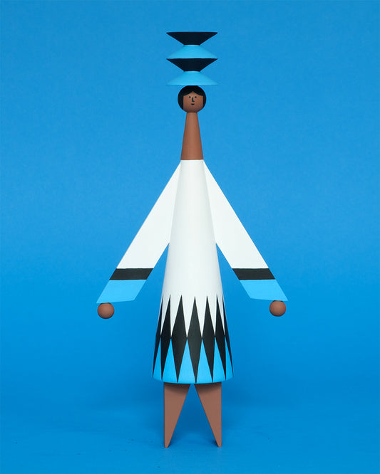 A colourful sculpture with a black, white and blue diamond patterned dress with brown legs and a matching blue and black headdress on a plain blue background.