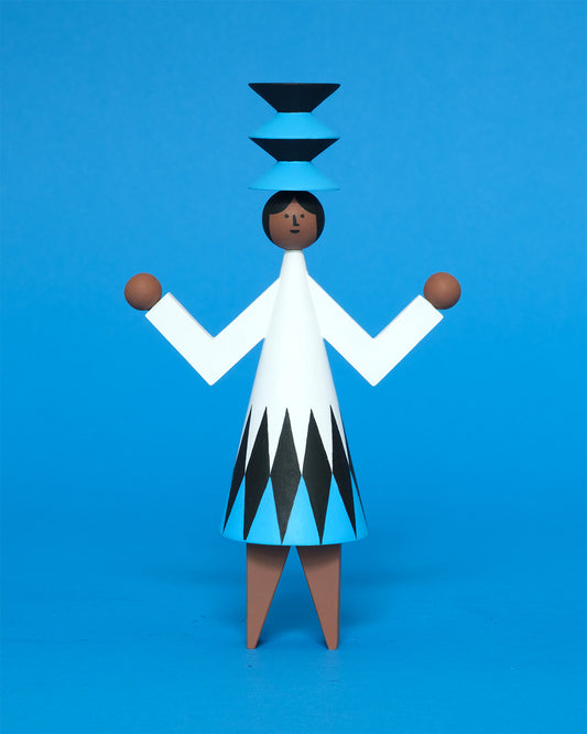 A colourful wooden sculpture with a black, white and blue diamond patterned dress with brown legs and a matching blue and black headdress on a plain blue background.