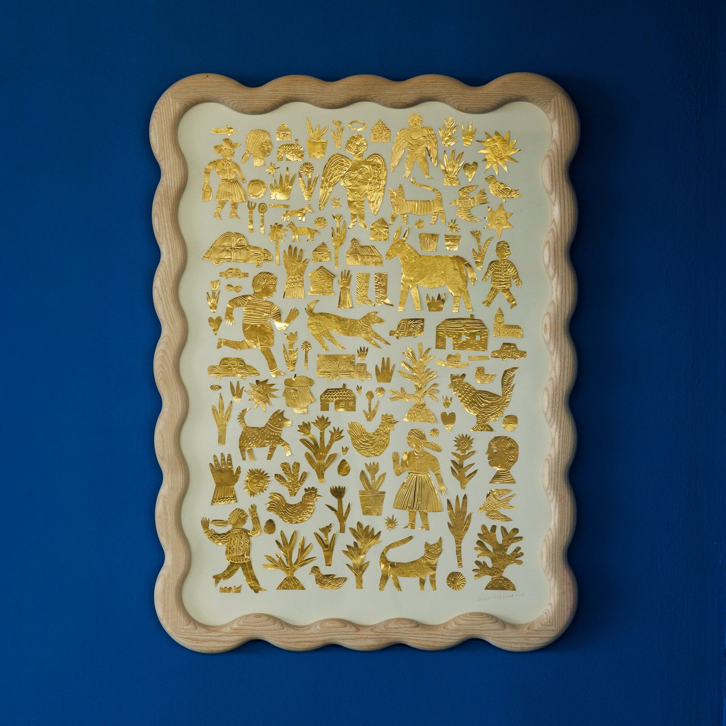 A decorative wall art piece featuring intricate gold foil illustrations on a cream background. The designs include various animals, plants, and human figures, all framed in a scalloped wooden border, set against a deep blue wall.