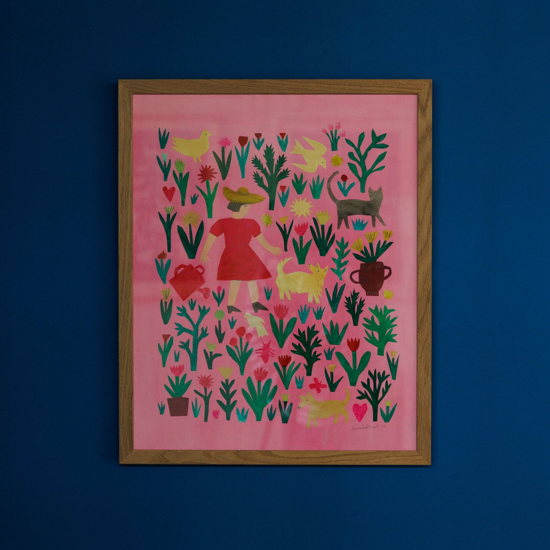 A framed artwork featuring a vibrant pink background adorned with various plants, animals, and a red dress. The design includes stylised shapes of birds, hearts, and pots, all set against a deep blue wall.