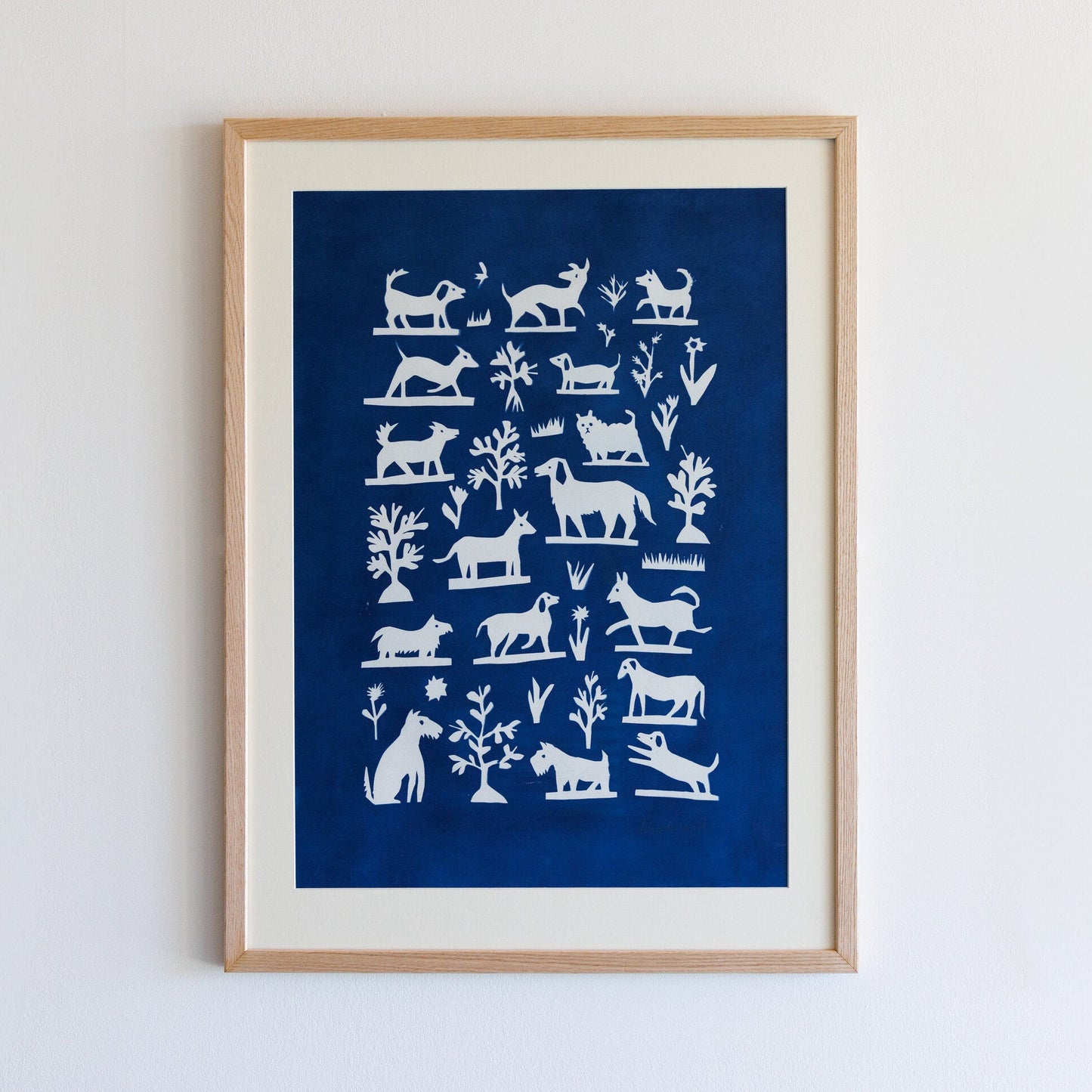 A framed artwork featuring a collection of white silhouettes of various animals and plants against a deep blue background. The design includes stylised representations of dogs, cats, and other creatures, arranged in a grid pattern.