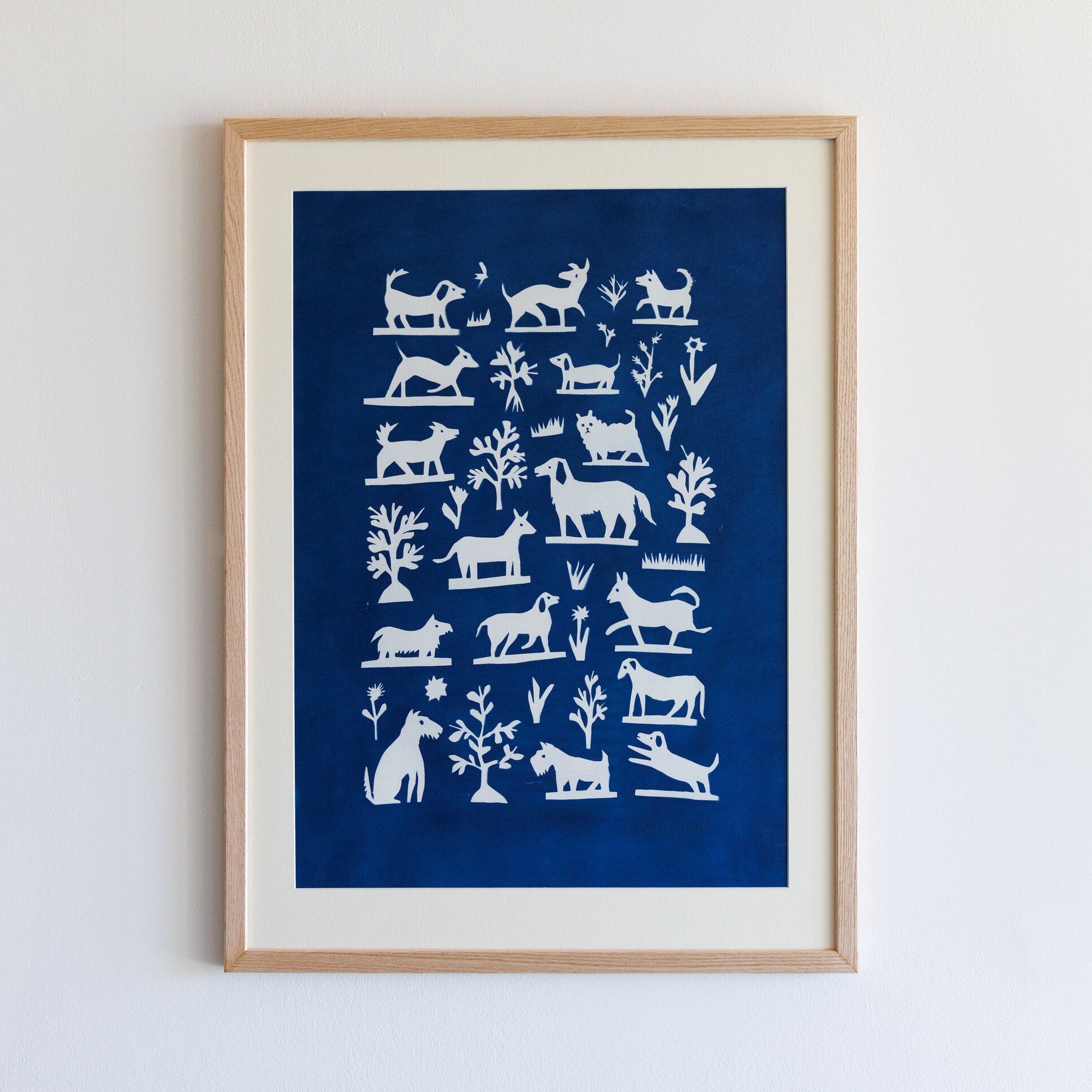 A framed artwork featuring a collection of white silhouettes of various animals and plants against a deep blue background. The design includes stylised representations of dogs, cats, and other creatures, arranged in a grid pattern.