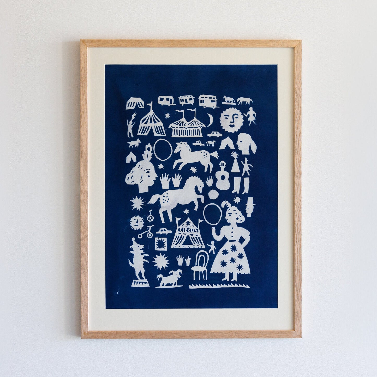 A framed artwork featuring a collection of white silhouettes on a deep blue background. The designs include circus scenes, animals like horses and dogs, musical instruments, and whimsical figures, creating a playful and vibrant composition.