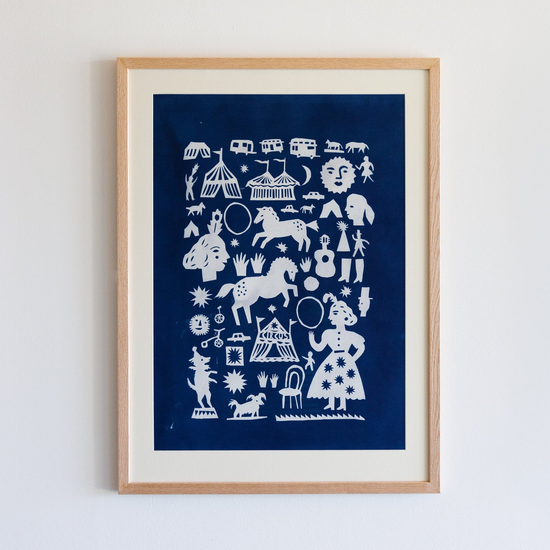 A framed artwork featuring a collection of white silhouettes on a deep blue background. The designs include circus scenes, animals like horses and dogs, musical instruments, and whimsical figures, creating a playful and vibrant composition.