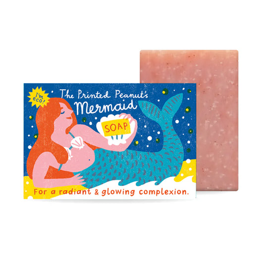 A vibrant illustration of a mermaid holding a bar of soap, set against a starry background. The packaging features playful text promoting the soap for a radiant and glowing complexion, with a pink bar of soap beside it.