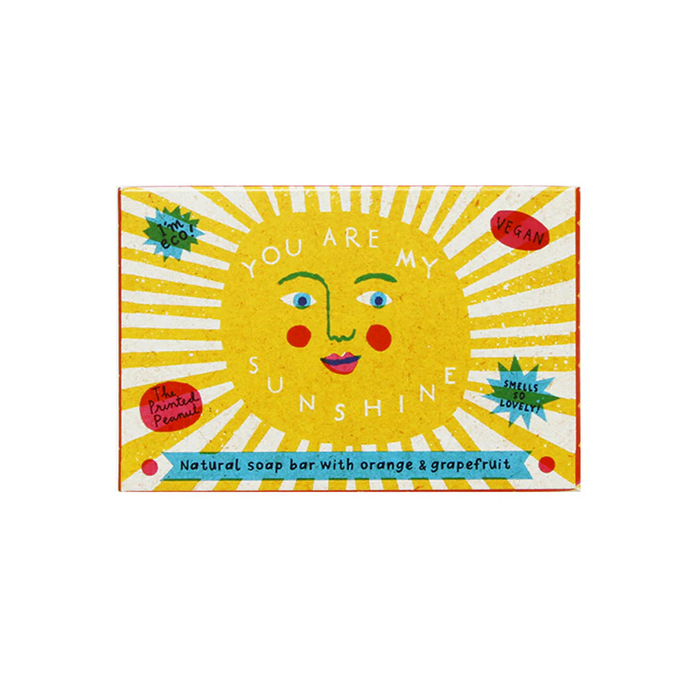 A vibrant soap bar packaging featuring a cheerful sun face with the text "You Are My Sunshine." The box is decorated with bright yellow rays and red accents, highlighting its vegan formula with orange and grapefruit scents.