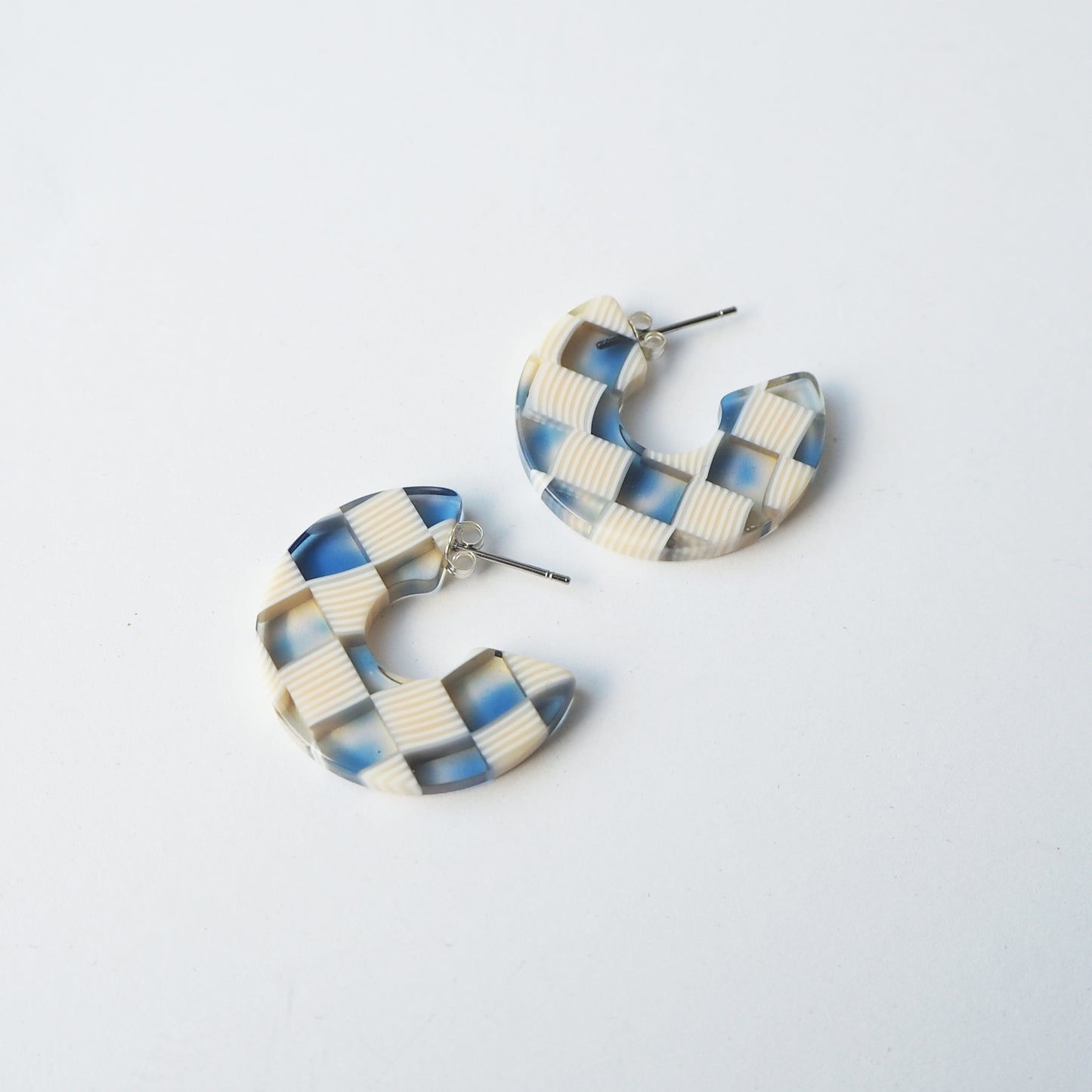 Pair of larger blue and beige checkered hoop earrings on a light grey background