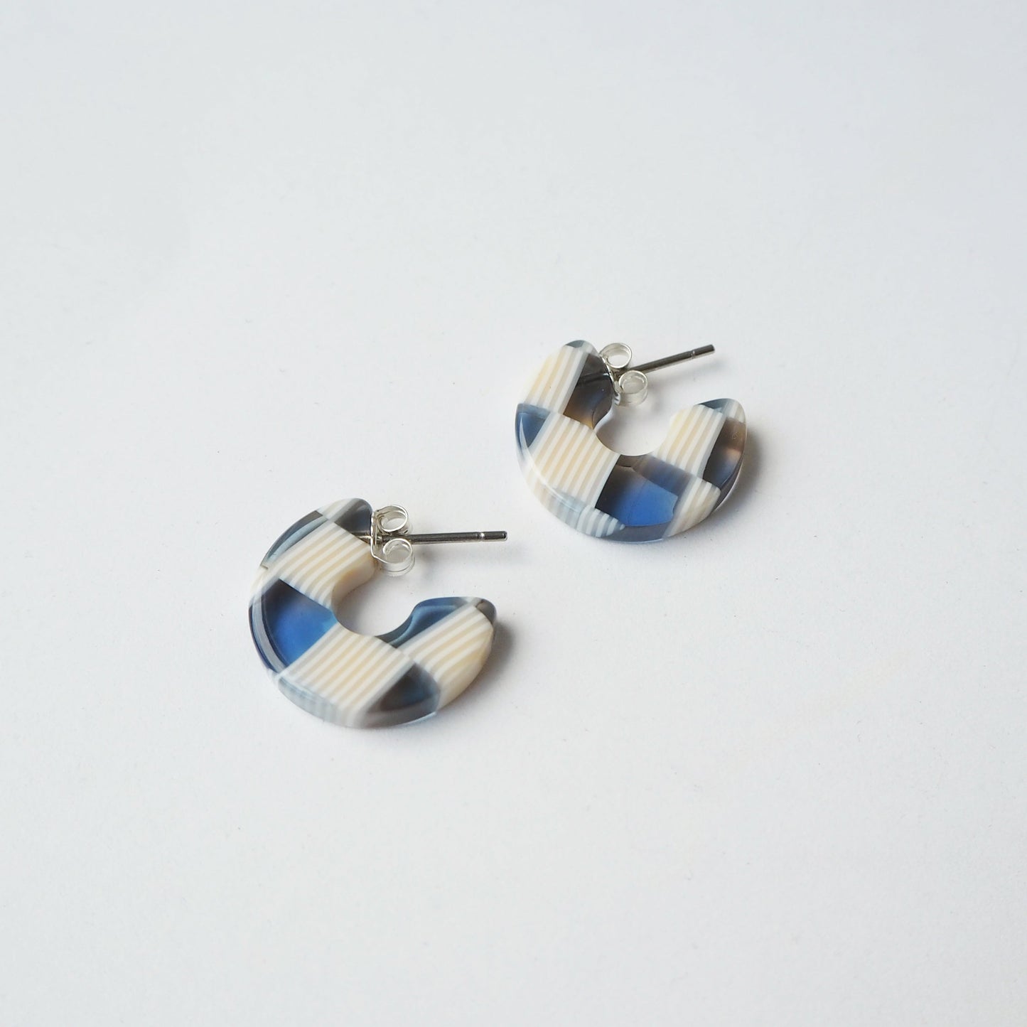 Pair of beige and blue checkered earrings on a light grey background