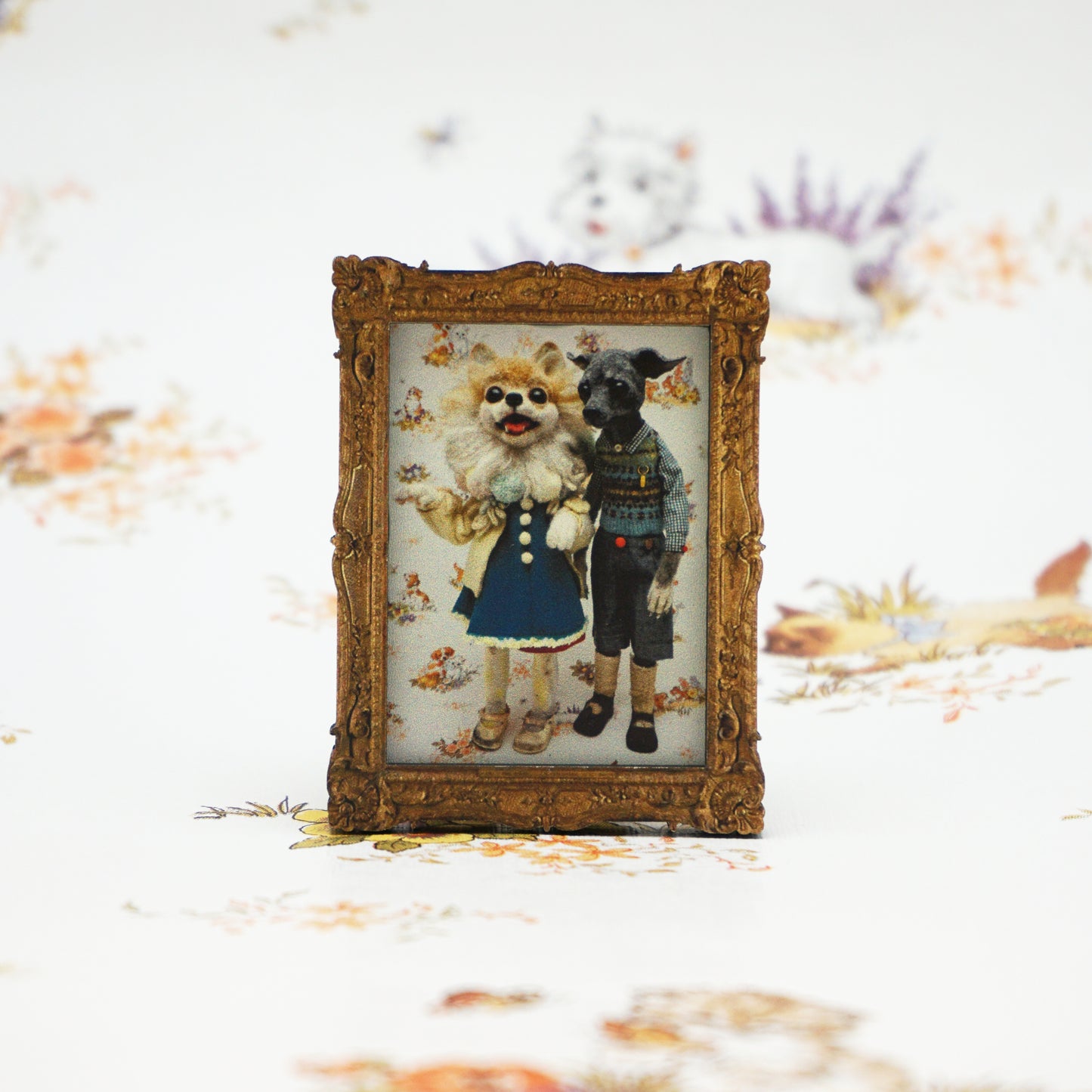 A small, ornate gold frame holds a whimsical illustration of two anthropomorphic animals dressed in vintage clothing. The background features a soft, floral pattern, adding a charming, nostalgic feel to the scene.