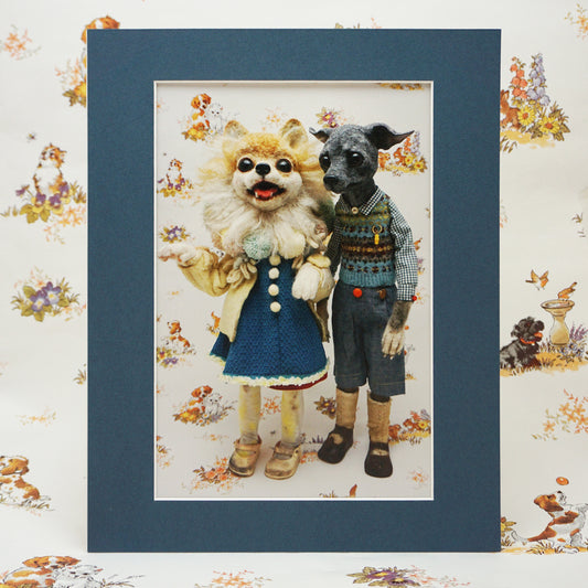 A mini print of two anthropomorphic animals: a fluffy dog in a blue dress with a white collar and a grey dog in a checked shirt, knitted vest, and trousers. The background features a floral and animal pattern. The print has a blue coloured mount.