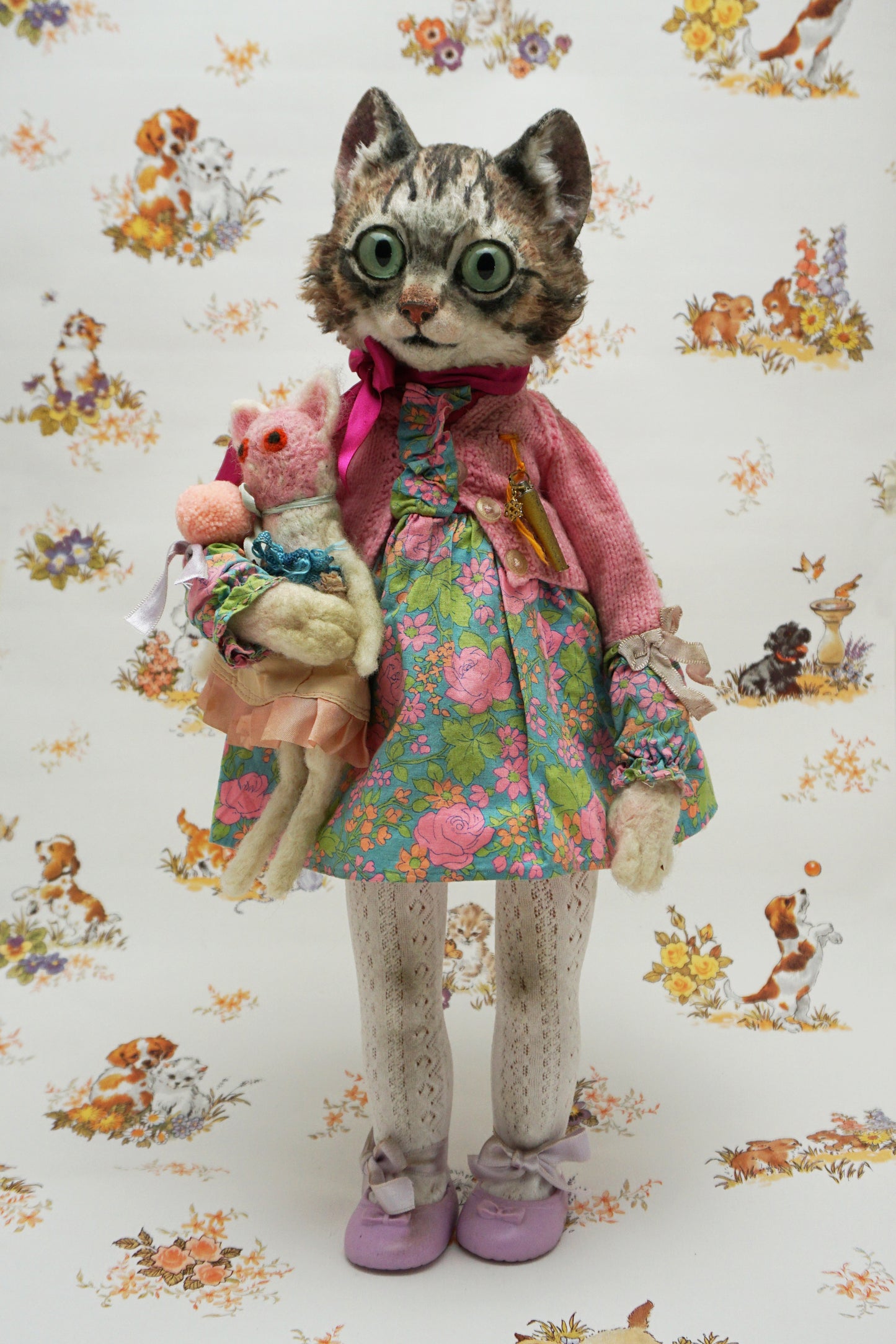A whimsical cat doll dressed in a floral dress, pink cardigan, and purple shoes holds a smaller plush toys. The background features playful animal illustrations, adding a charming, vintage feel to the scene.