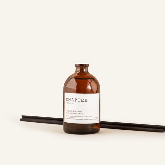 A brown glass bottle labelled "CHAPTER ORGANICS" sits on a light background. Two black incense sticks lie beside the bottle, creating a minimalist and calming aesthetic.