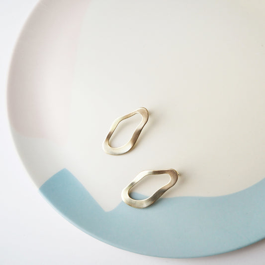 Wavy round gold stud earrings sitting on a blue and beige plate