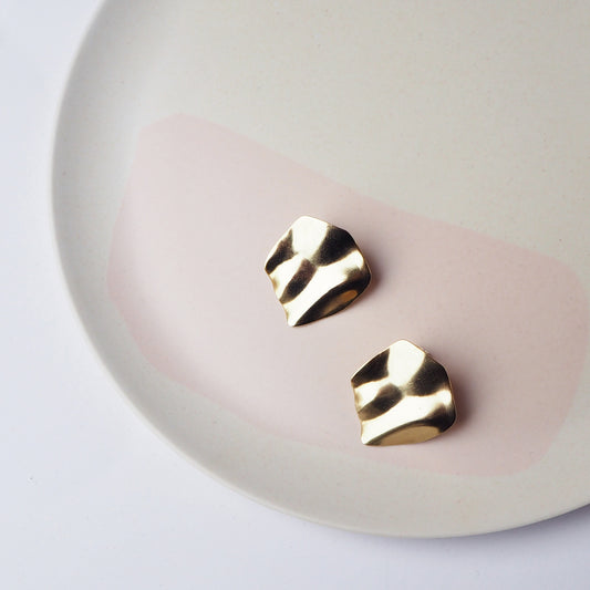 Round gold abstract stud earrings on a pale pink plate.