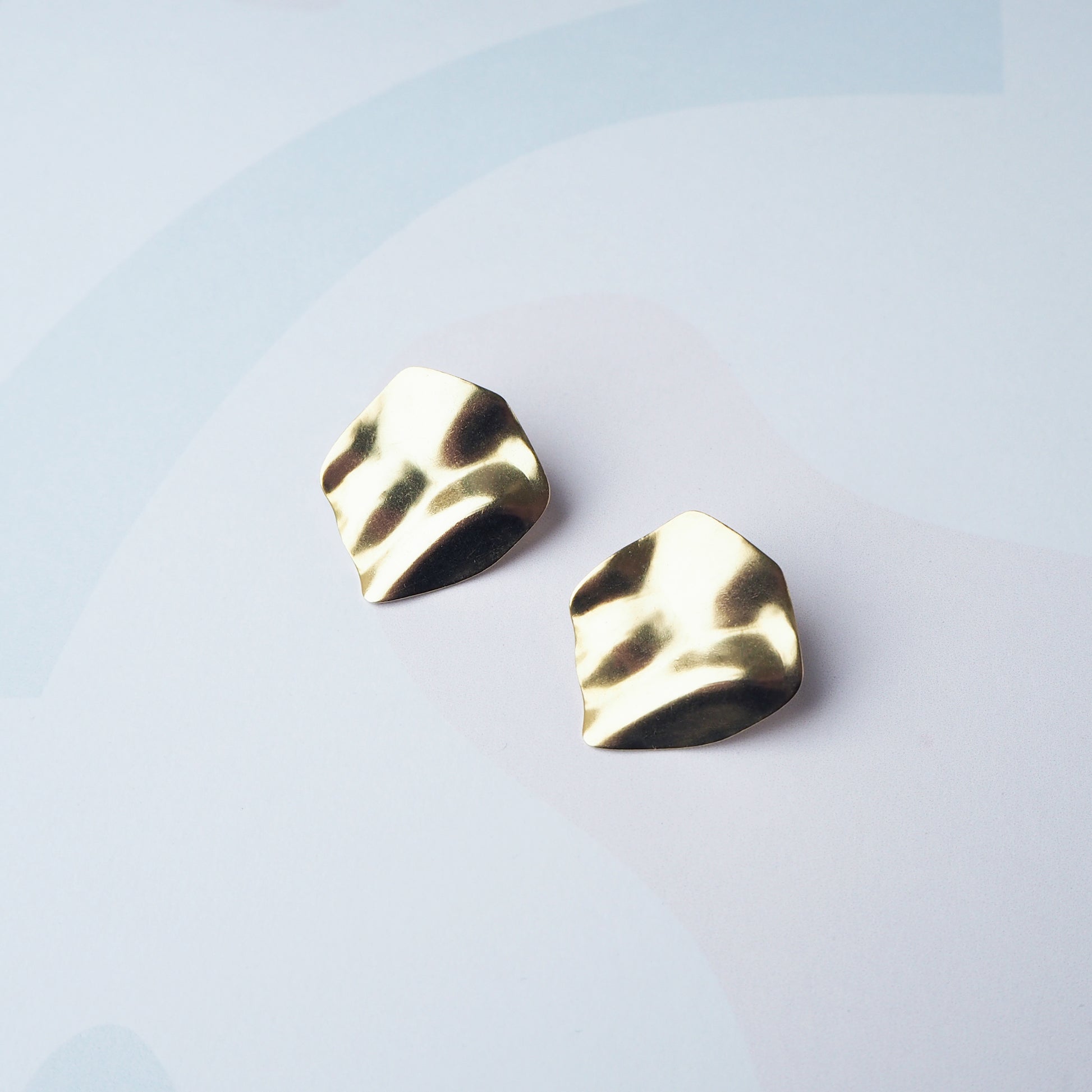 Round gold abstract earrings on a plain grey background