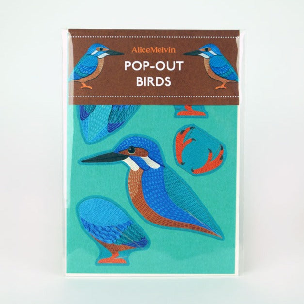 A colourful packaging featuring pop-out bird designs by Alice Melvin. The background is turquoise, showcasing stylised illustrations of birds in various poses, with a brown label at the top stating "POP-OUT BIRDS".