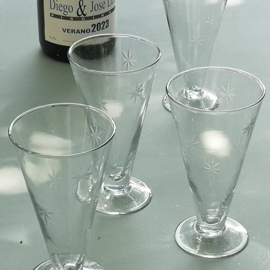 Four clear prosecco glasses on a light grey surface with a bottle labelled 'Diego & Jose Luis Verano 2023'.