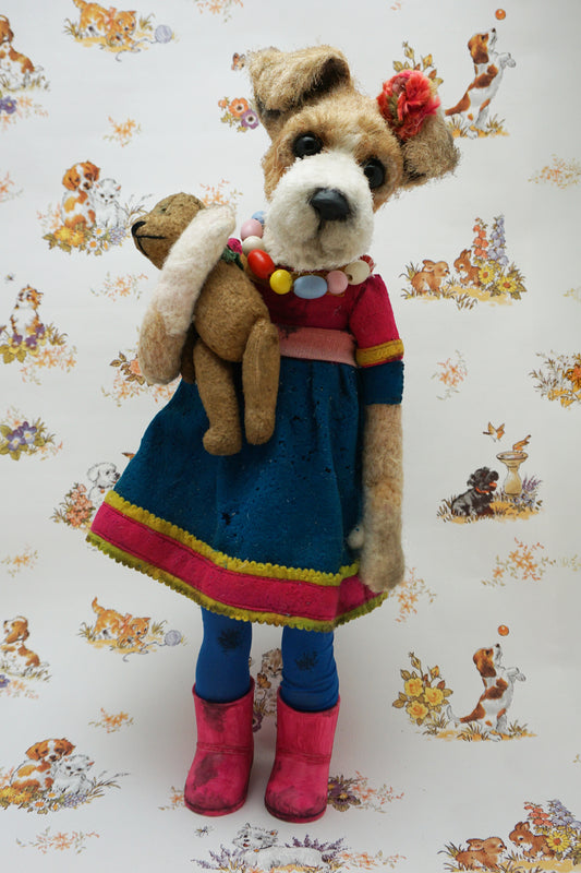 A plush dog dressed in a blue dress with pink trim, colourful bead necklace, and pink boots, holding a smaller plush bear. The background features a pattern of various playful animals and floral designs.