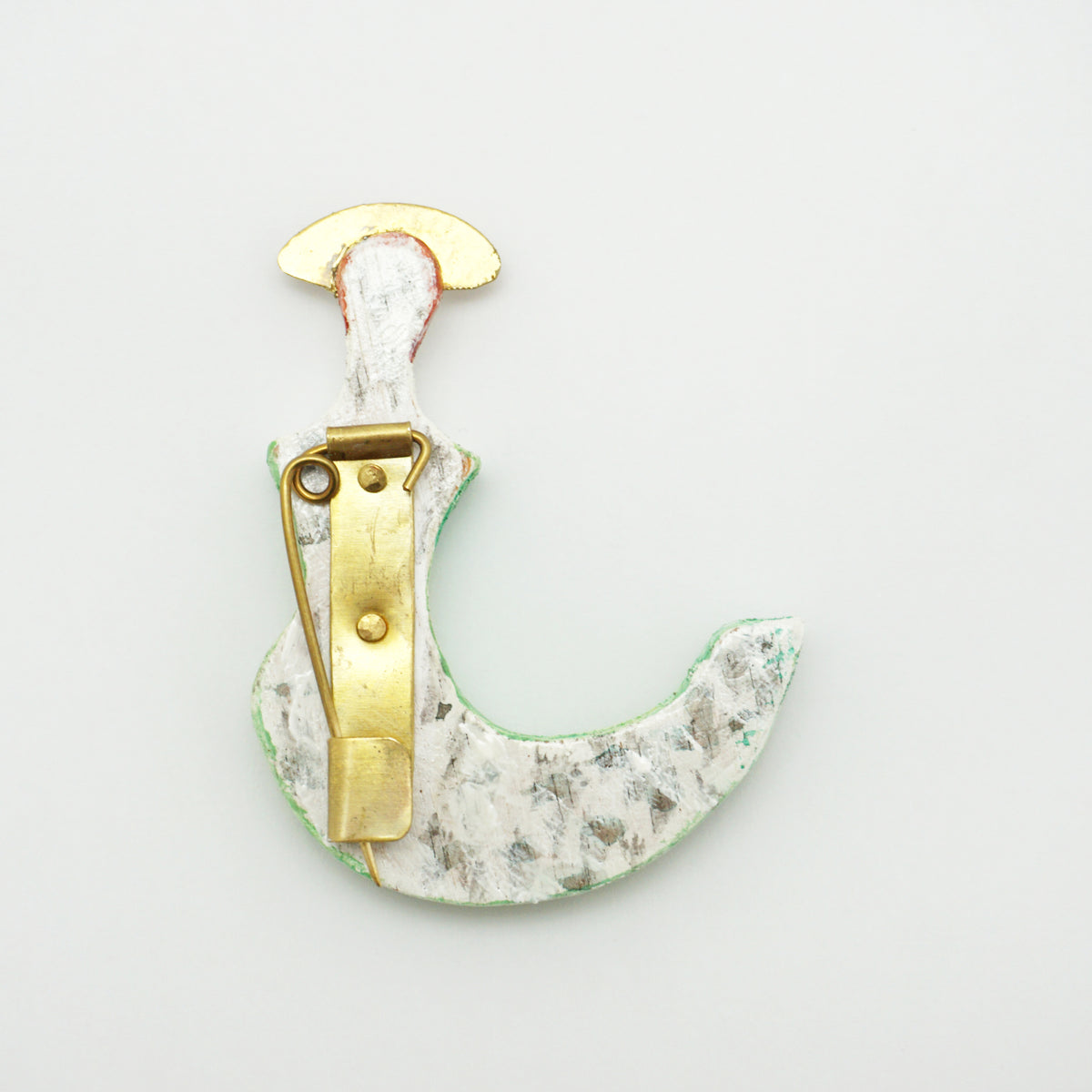 The back of a whimsical crescent-shaped brooch showing a gold pin fastenings. 
