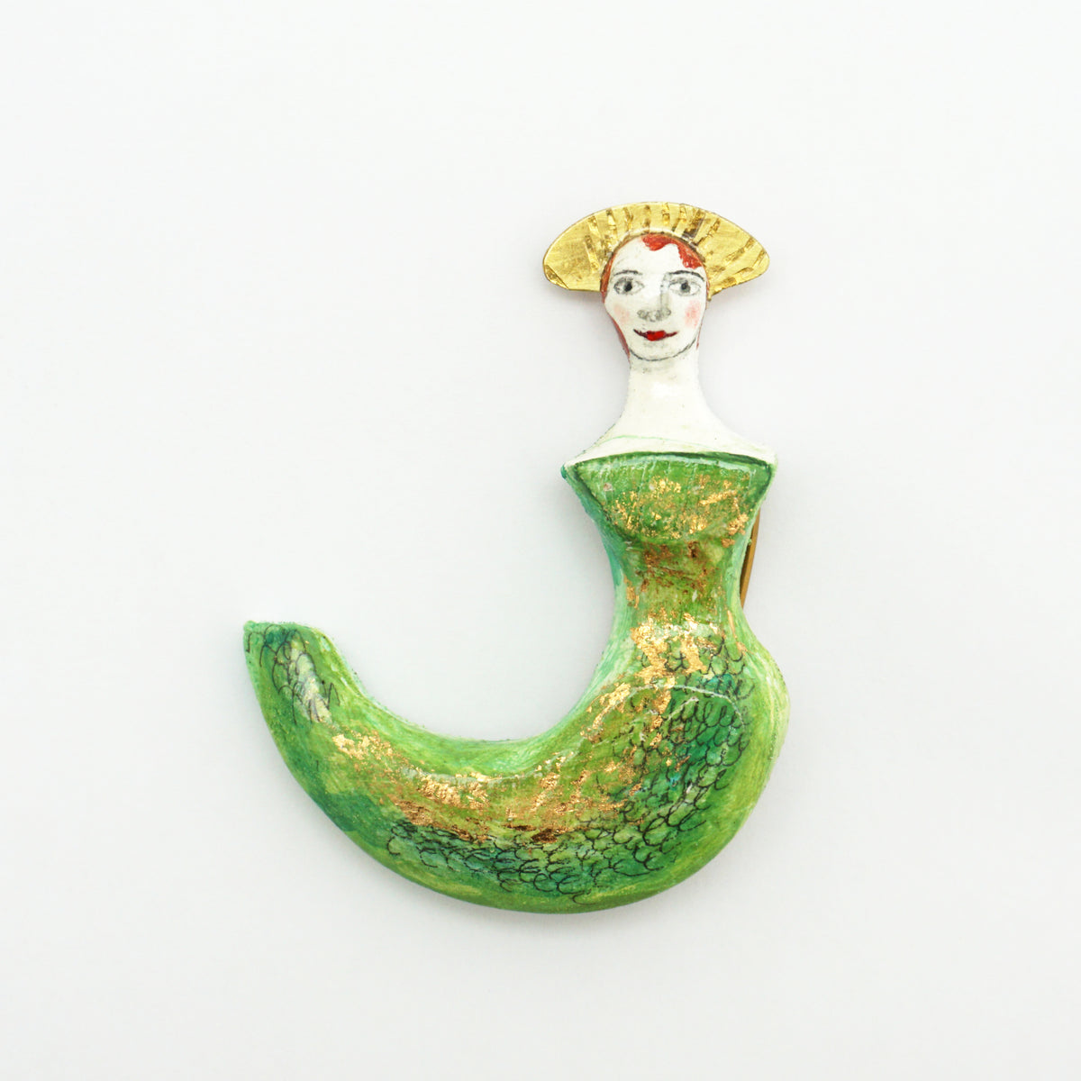 A whimsical crescent-shaped brooch or pin depicting a woman in a green dress with gold glitter accents, a white neck, and a yellow fan-like hairpiece, shown on a plain white background.
