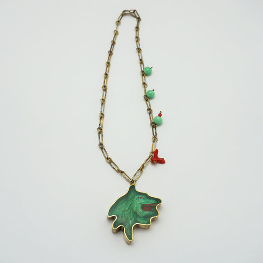 A vintage-style necklace featuring a gold-tone chain, small turquoise-green beads, a tiny red coral charm, and a large green pendant with a gold-tone outline, displayed on a clean white background.