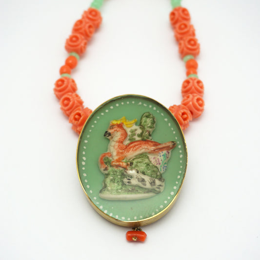Necklace with an oval hand painted pendant insert that features an animal design on a green background. The necklace chain is made up of orange and green rose shapes Bakelite beads. 