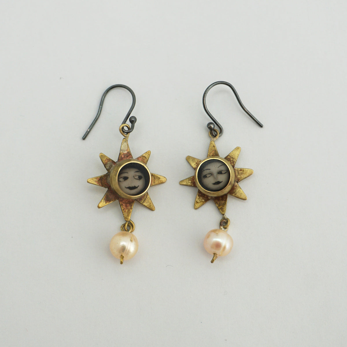 A pair of vintage-style dangle earrings featuring sunburst charms with miniature portrait medallions and dangling pearl-like beads, shown on a plain light background.