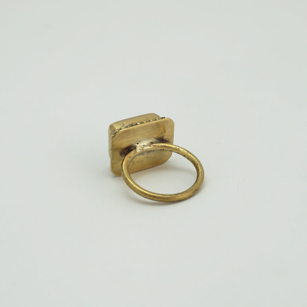 The back of a rectangular brass ring on a plain white background.