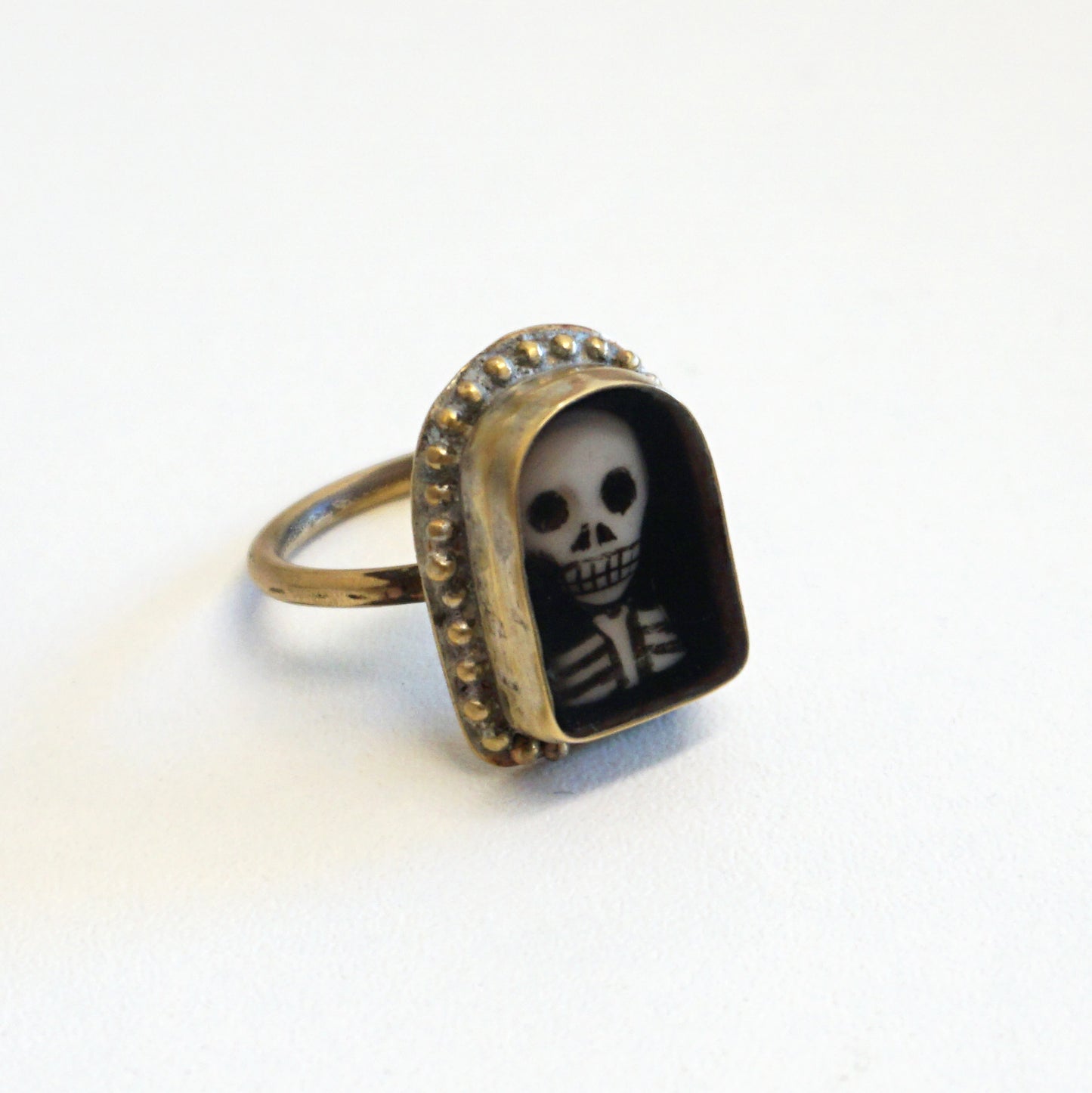 An arch shaped ring featuring a miniature portrait of a skeleton's head and shoulders.