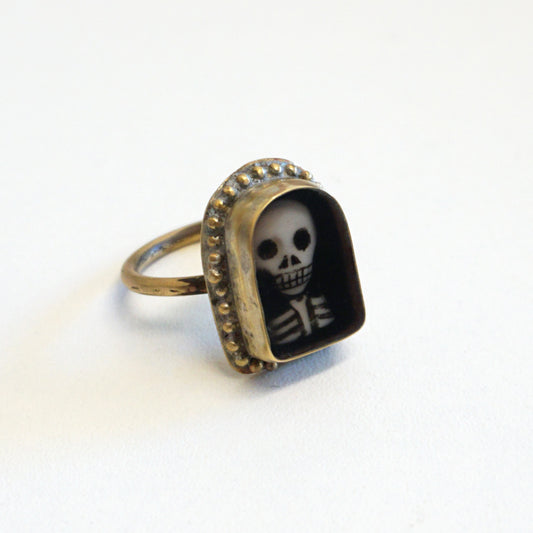 An arch shaped ring featuring a miniature portrait of a skeleton's head and shoulders.