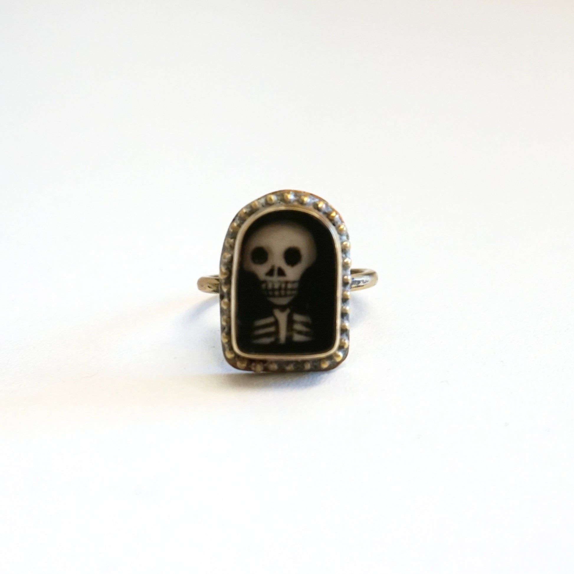 An arch shaped ring featuring a miniature portrait of a skeleton's head and shoulders.