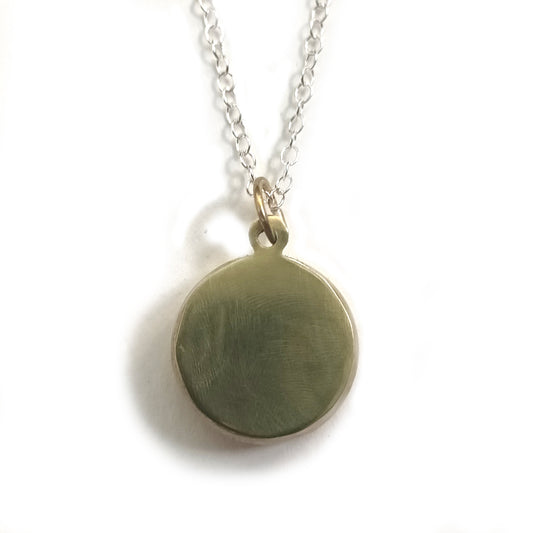 The back of a pendant, the surface is smooth and shiny, and is attached to a fine silver chain.