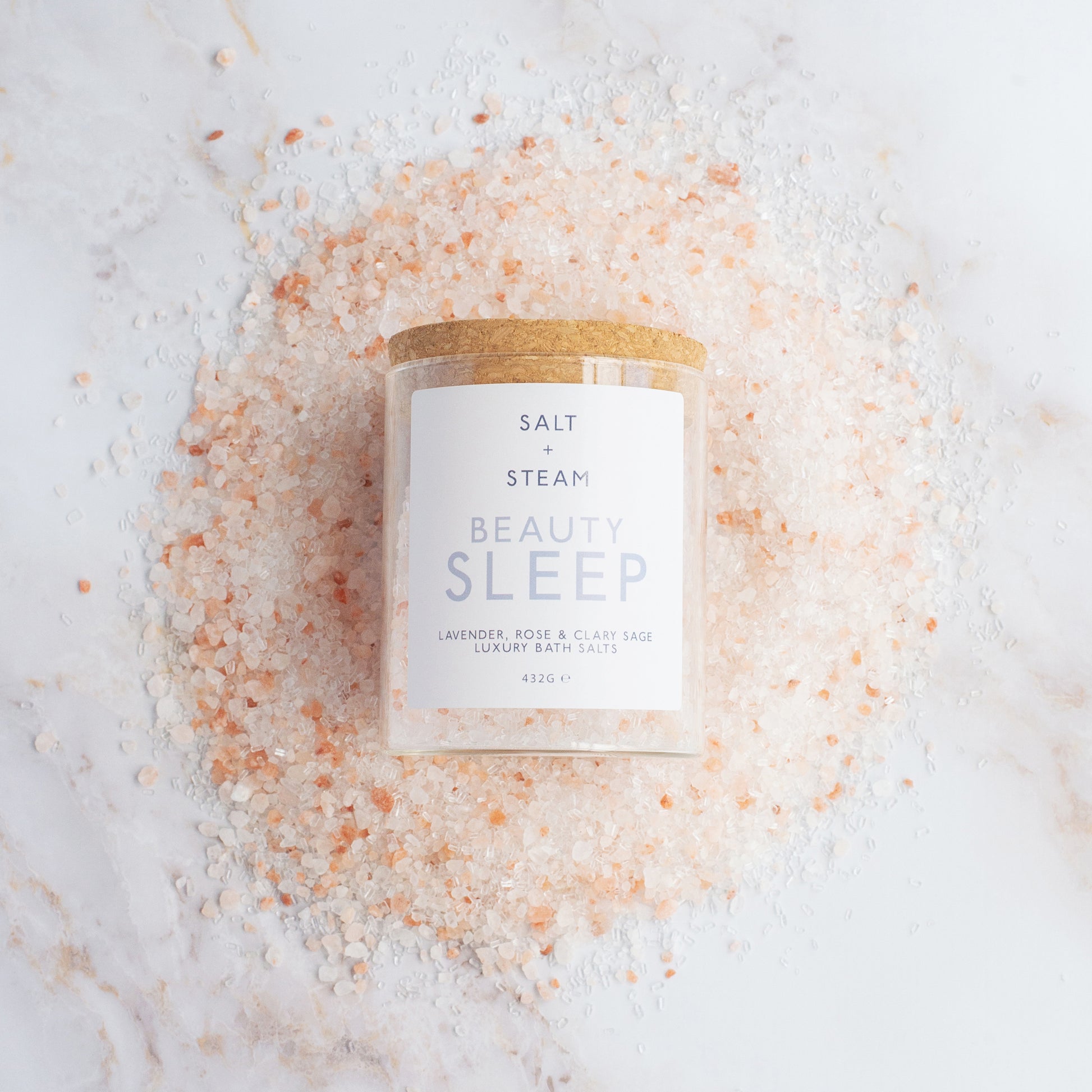 Glass jar labelled 'Beauty Sleep' surrounded by pink bath salt crystals on a white background.
