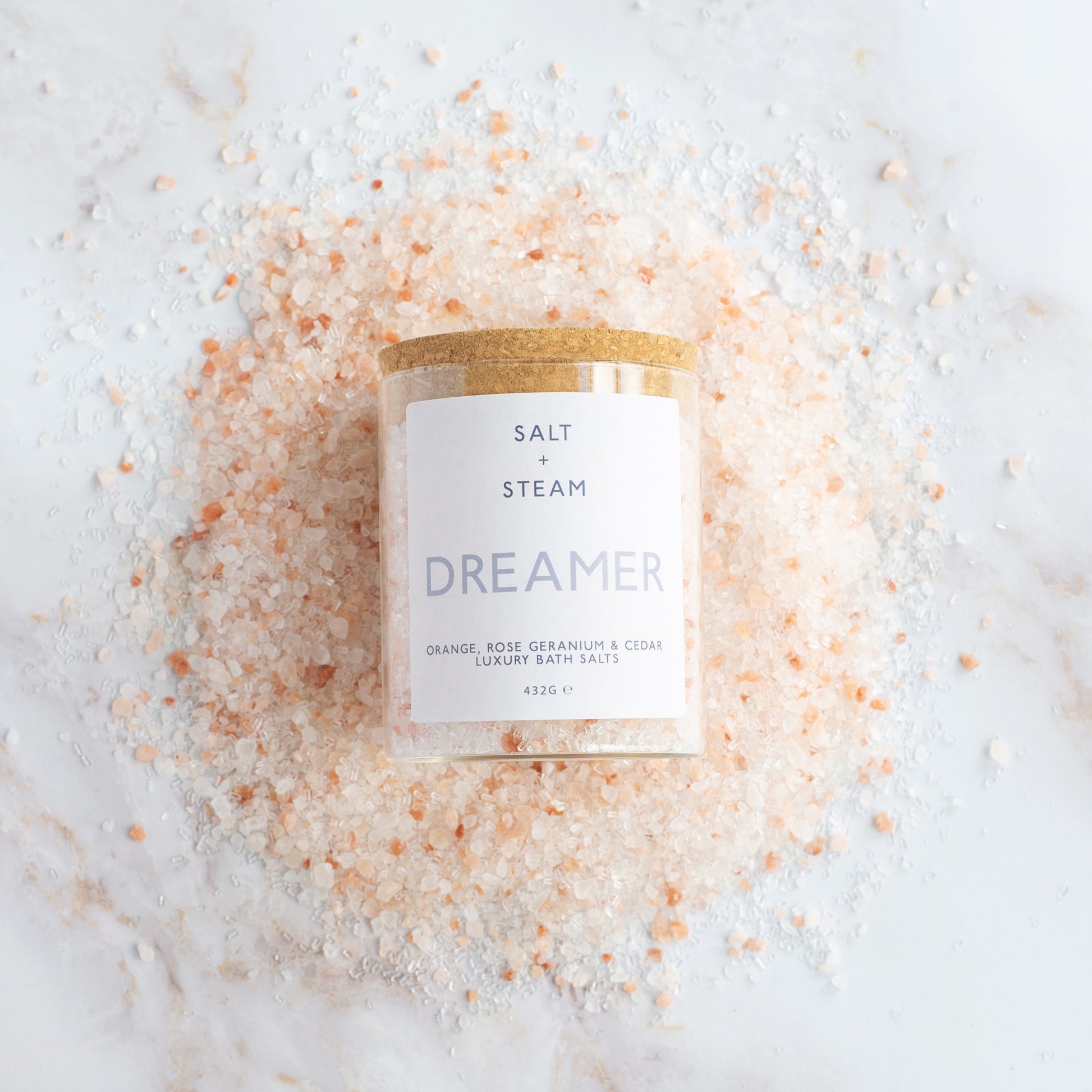 Bath salt container labeled 'Dreamer' surrounded by pink Himalayan salt crystals on a white background.