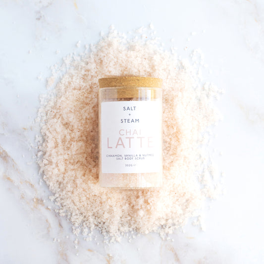 Jar of 'Chai Latte' salt scrub on a white surface with salt crystals around it.