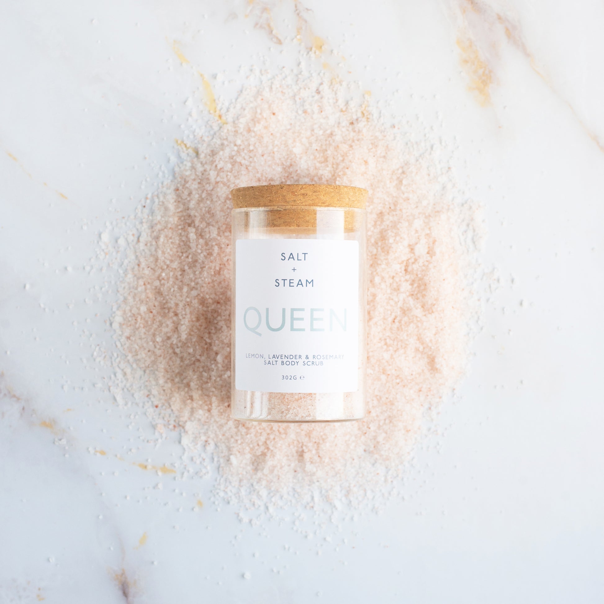 Body scrub jar labelled Queen surrounded by a decorative salt cloud on a light background
