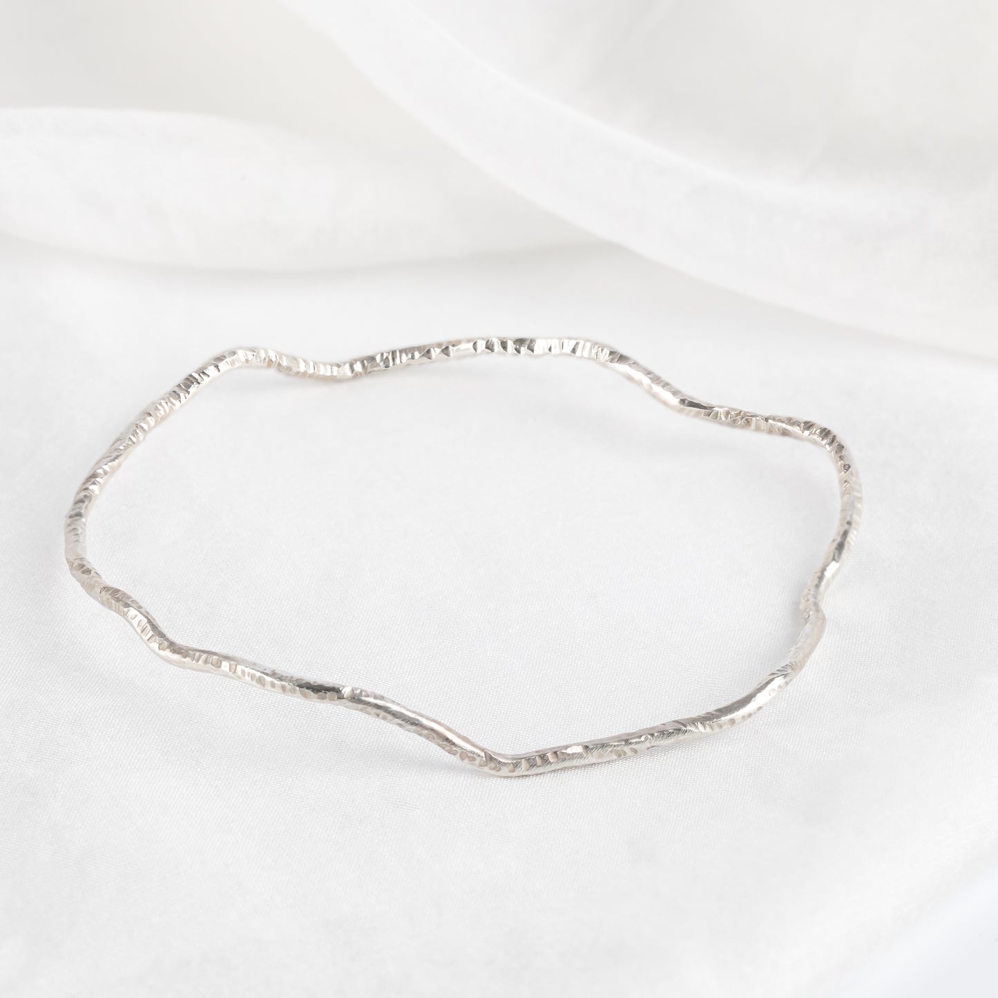 A silver bangle bracelet with a textured surface, displayed against a white background.