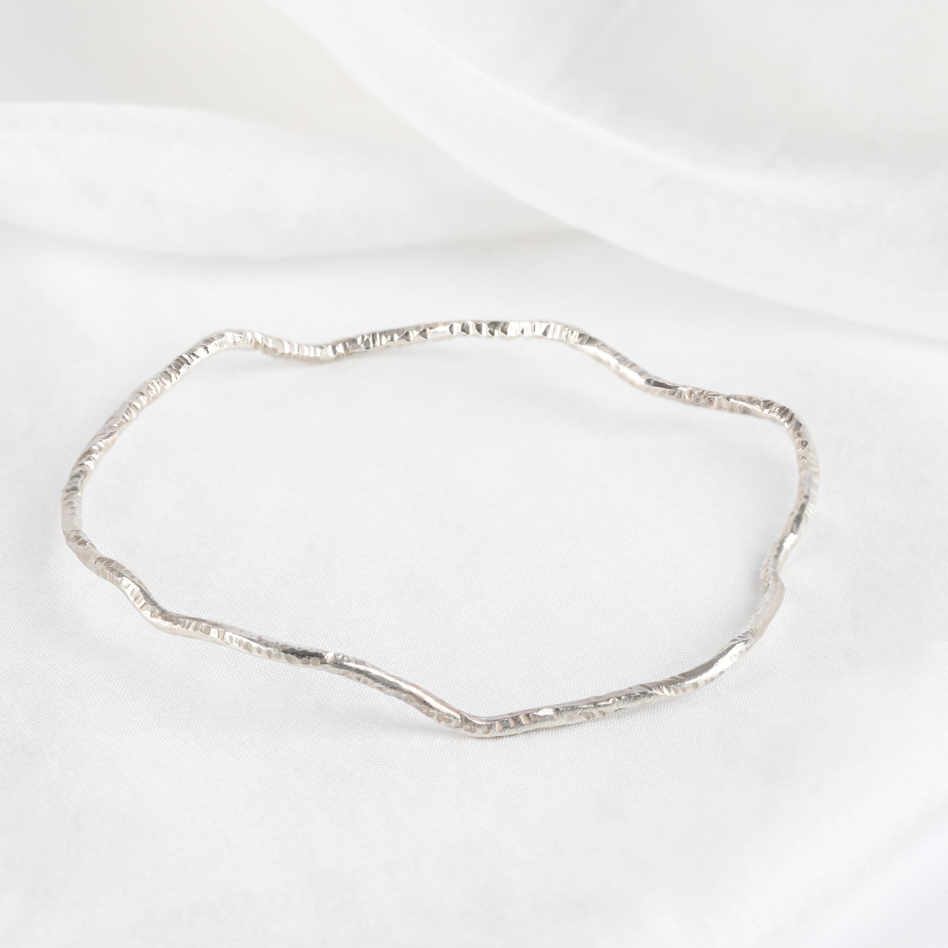 A silver bangle bracelet with a textured surface, displayed against a white background.
