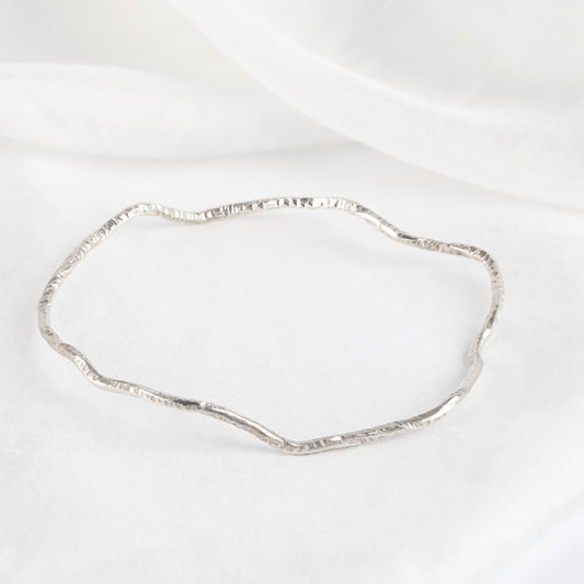 A silver bangle bracelet with a textured surface, displayed against a white background.