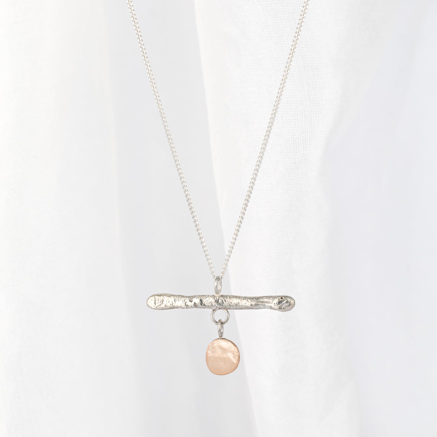 A silver bar pendant necklace with a gold drop, displayed against a light background.