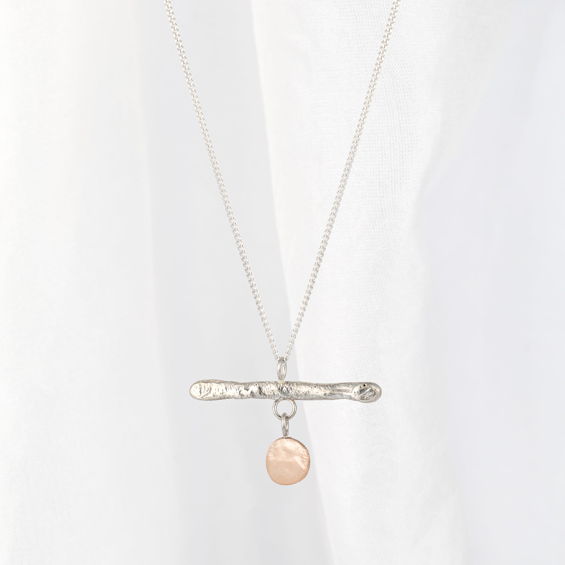 A silver bar pendant necklace with a gold drop, displayed against a light background.