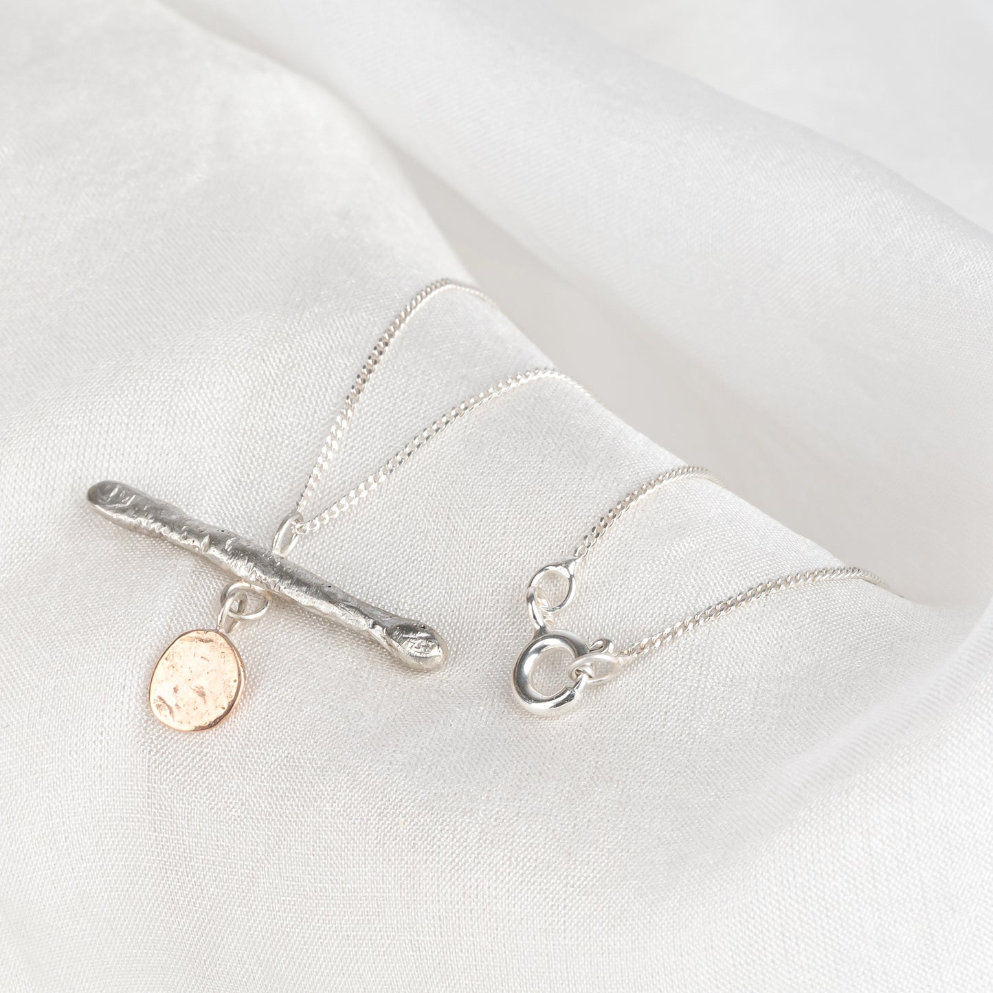 A silver bar pendant necklace with a gold drop, displayed against a light background.